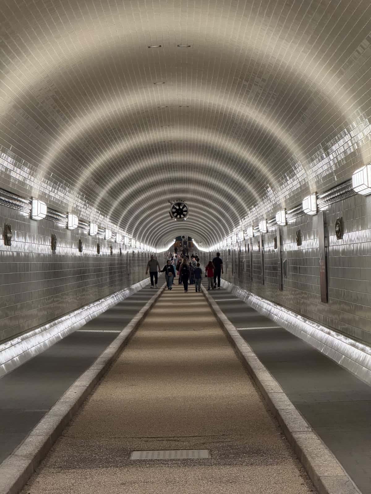 Pasillo de túnel alicatado en el St. Pauli-Elbtunnel con pocas personas al fondo e iluminación uniforme