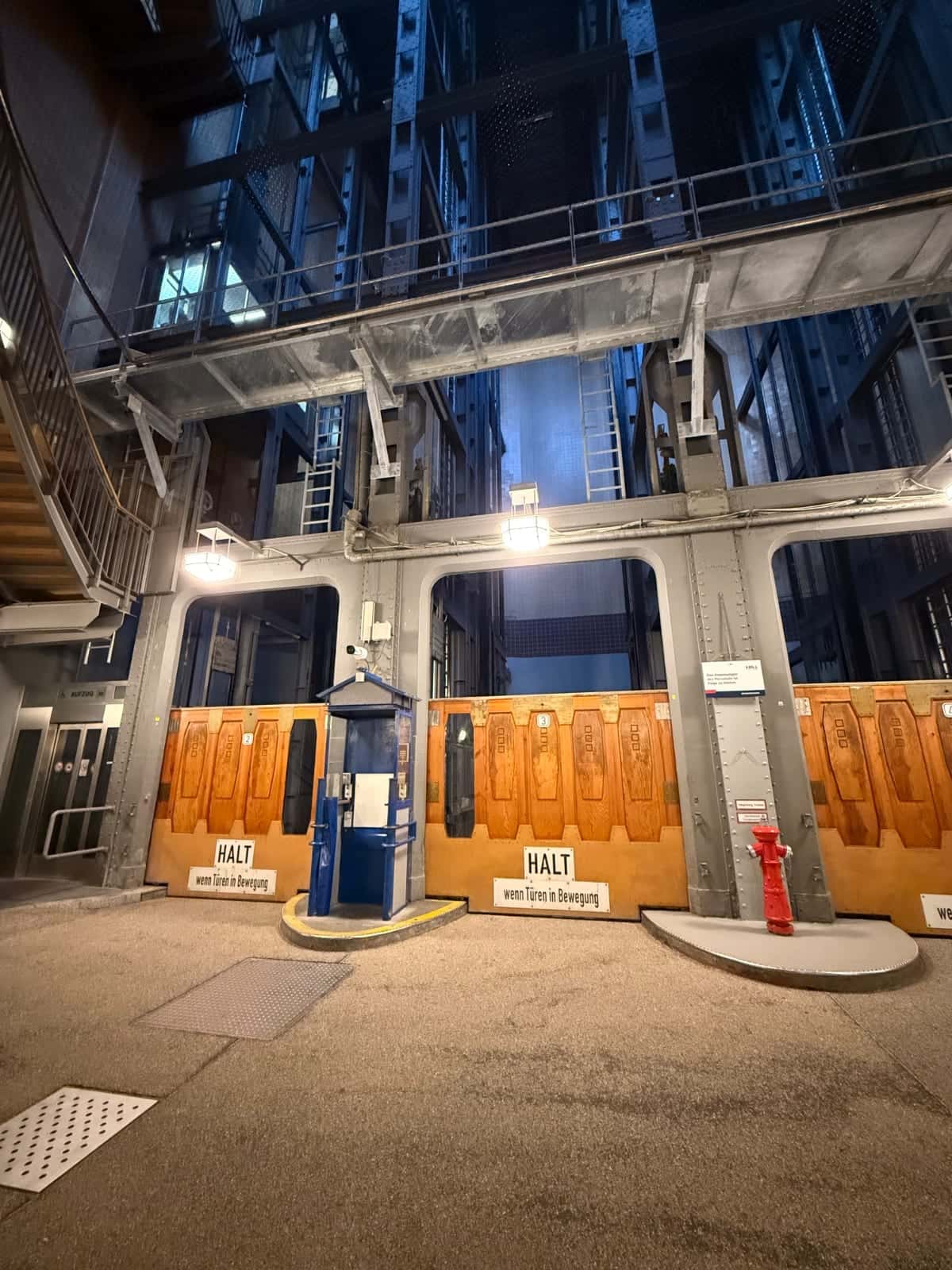 Patio en el St. Pauli-Elbtunnel con estructura metálica, puertas de madera, una pequeña cabina azul y blanca y una boca de incendios roja