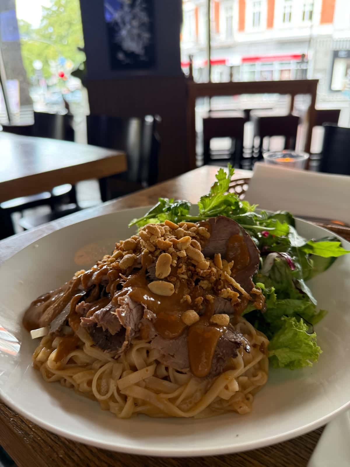 Un bol de fideos con carne, frutos secos y ensalada sobre una mesa junto a las ventanas en Phở Dàm