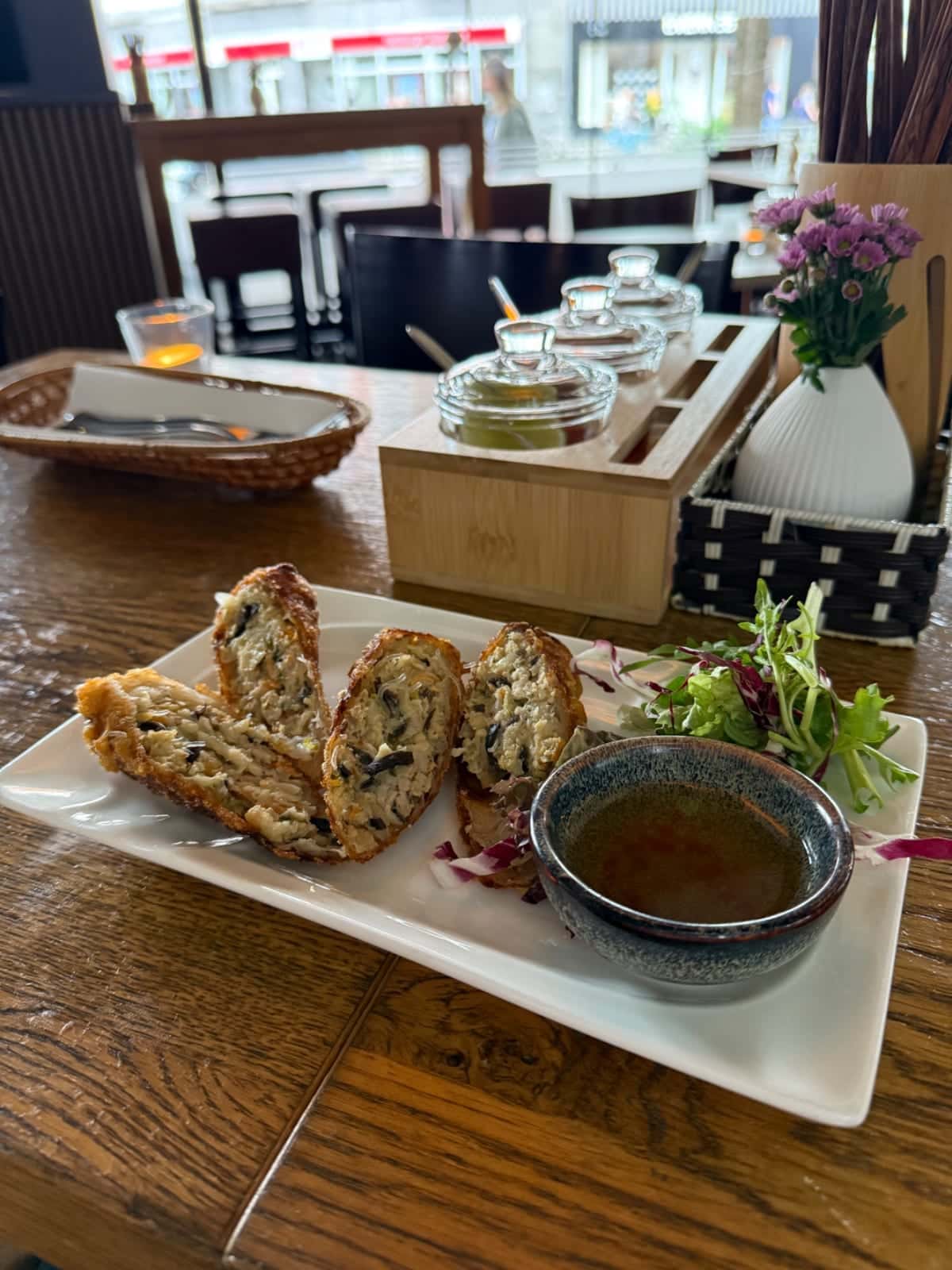 Rollos fritos con salsa para mojar en un plato en una mesa de restaurante en Phở Dàm, con ventanas y decoración de mesa al fondo