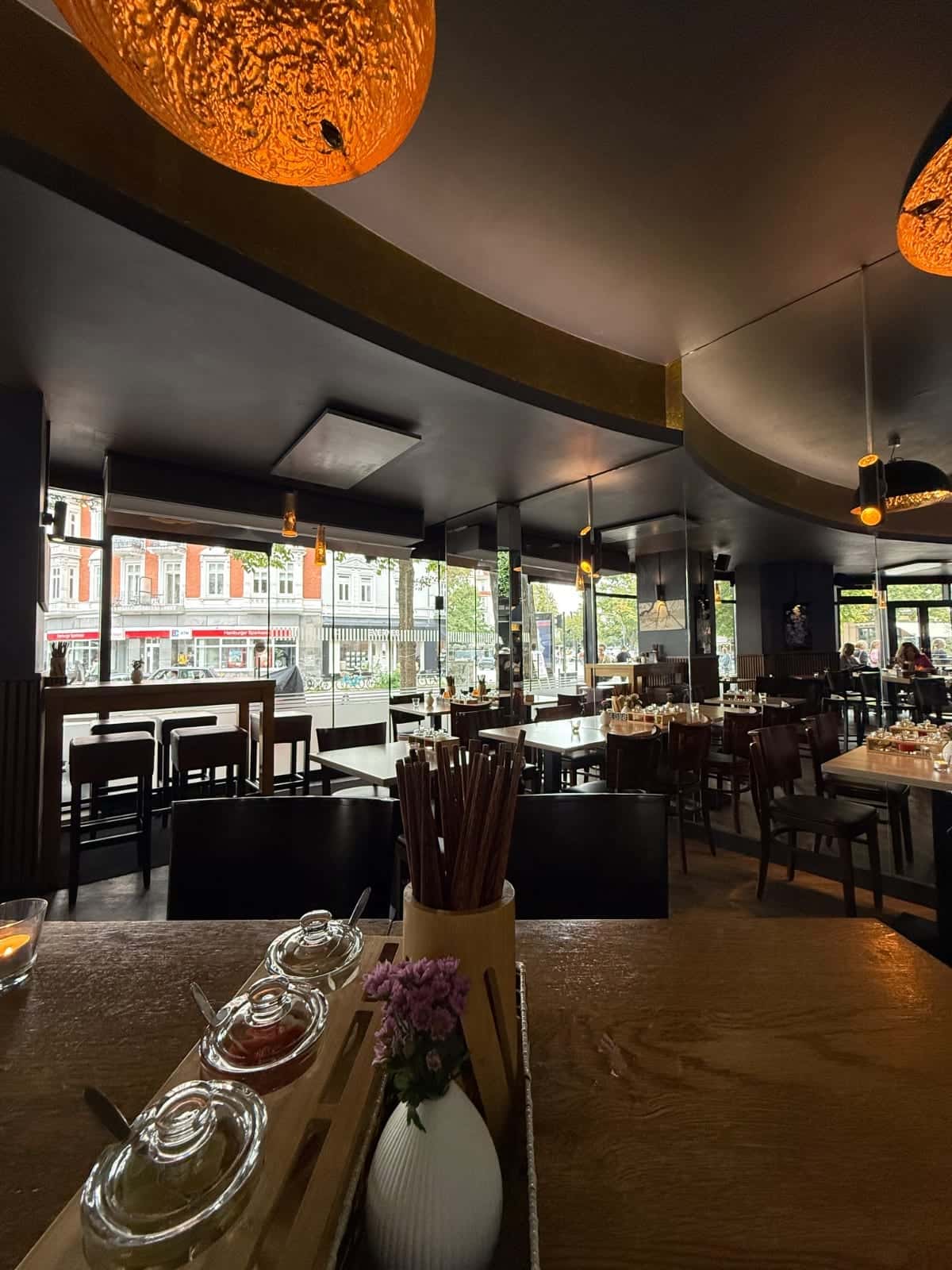 Interior de Phở Dàm con mesas, sillas y vista a la calle a través de grandes ventanales