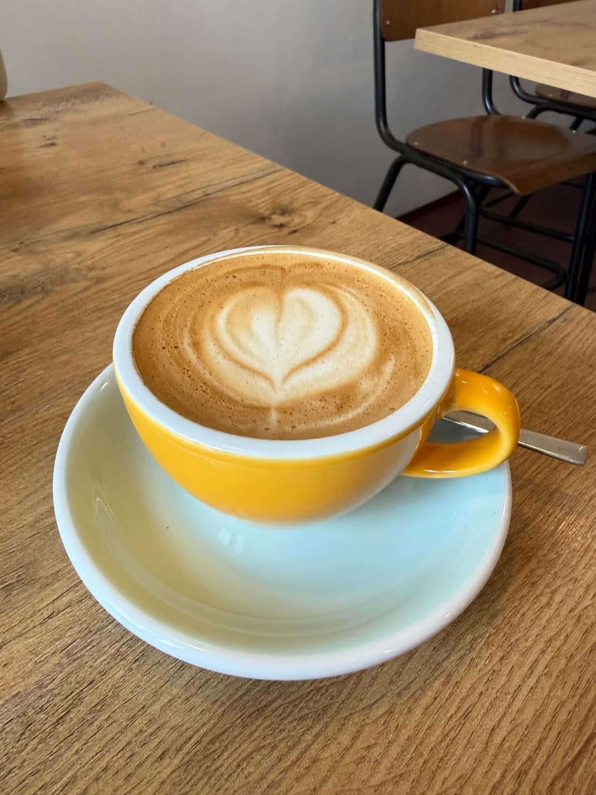 Taza amarilla con latte art sobre una mesa de madera en Café Mama Silvia