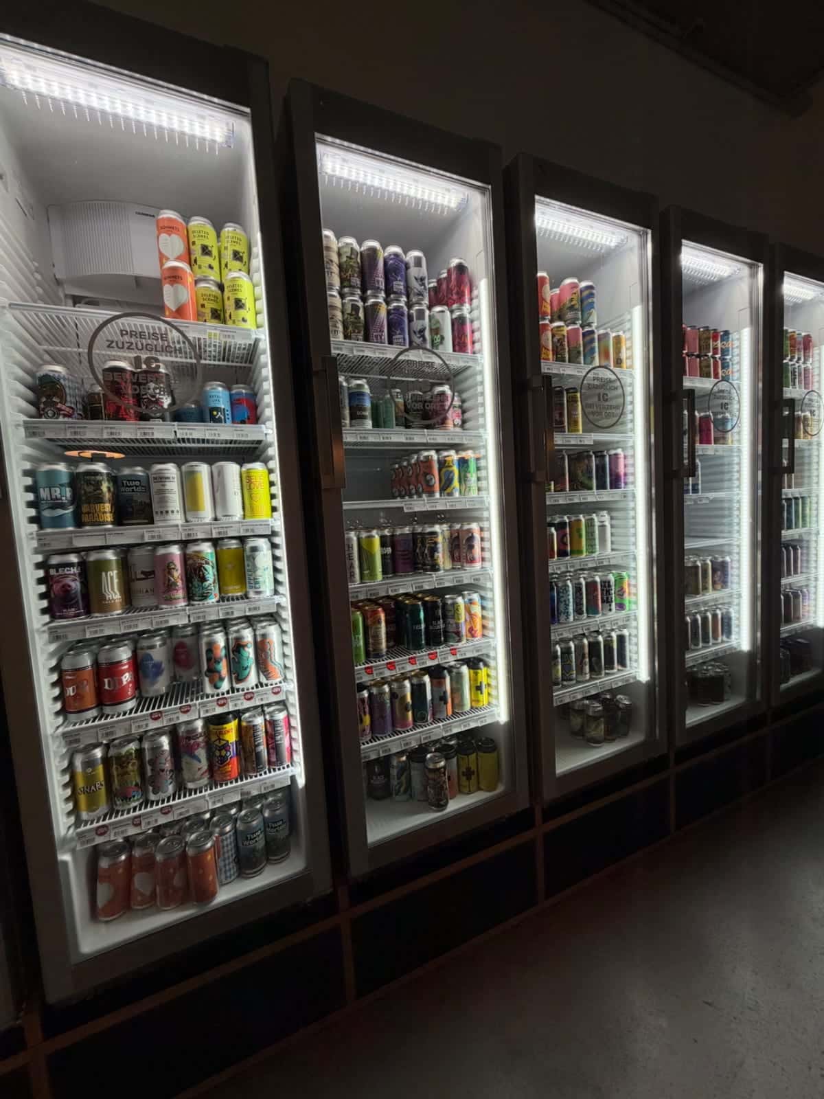 Varios refrigeradores iluminados con una gran selección de latas de bebidas en Beyond Beer