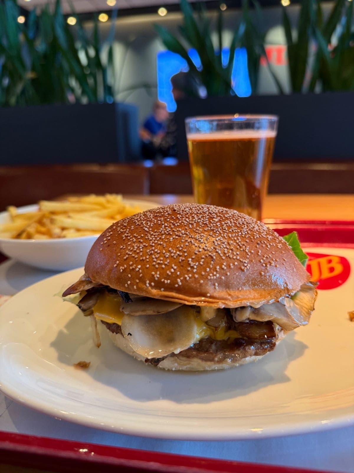 Hamburguesa con patatas fritas en un plato, con un vaso de cerveza al lado en Jim Block